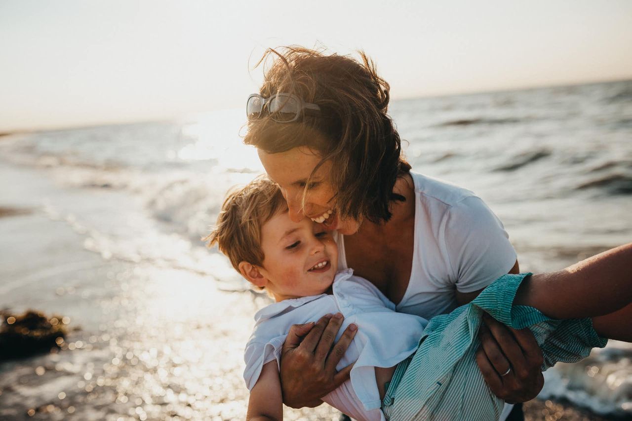 Mutter umarmt lachend ihr Kind am Strand